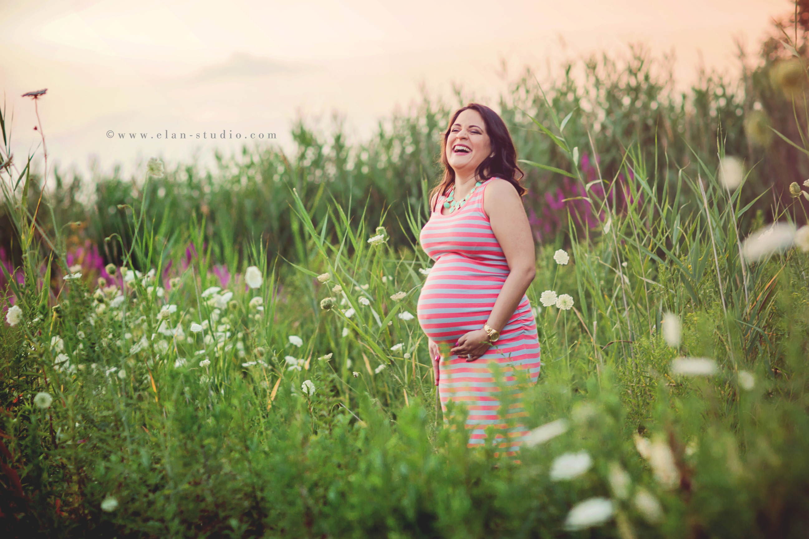 mother to be wearing striped dress and laughing in a field of wildflowers