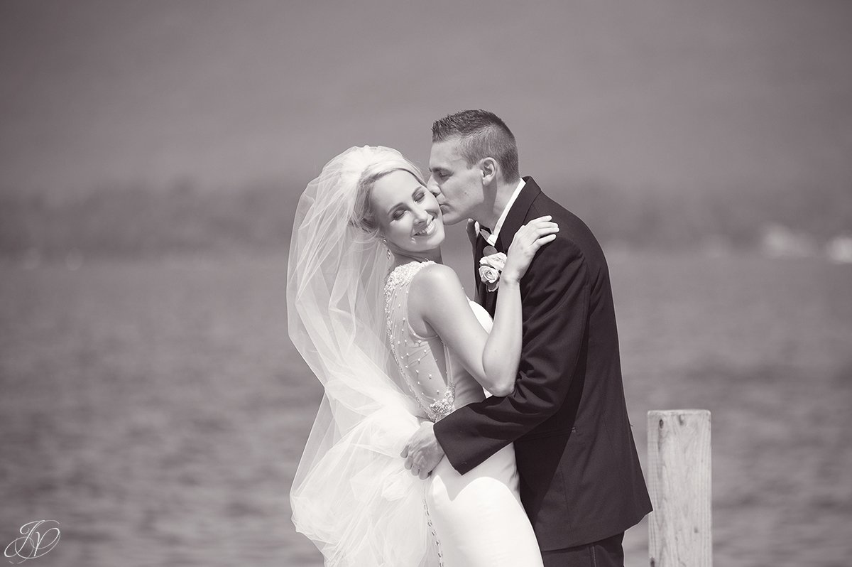 groom kissing bride cheek on lake black and white