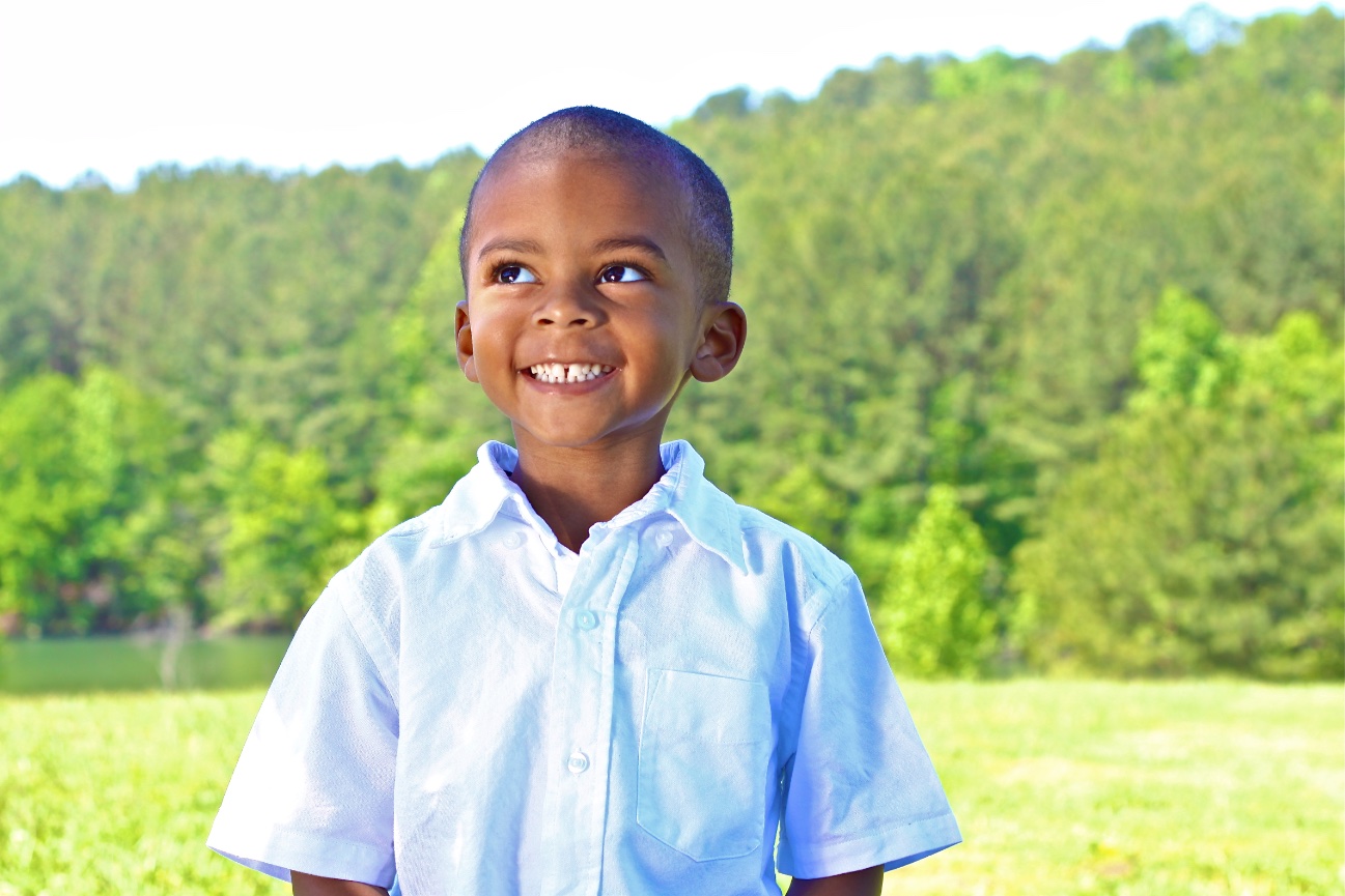 Smiling boy standing outdoors in front of a green landscape.