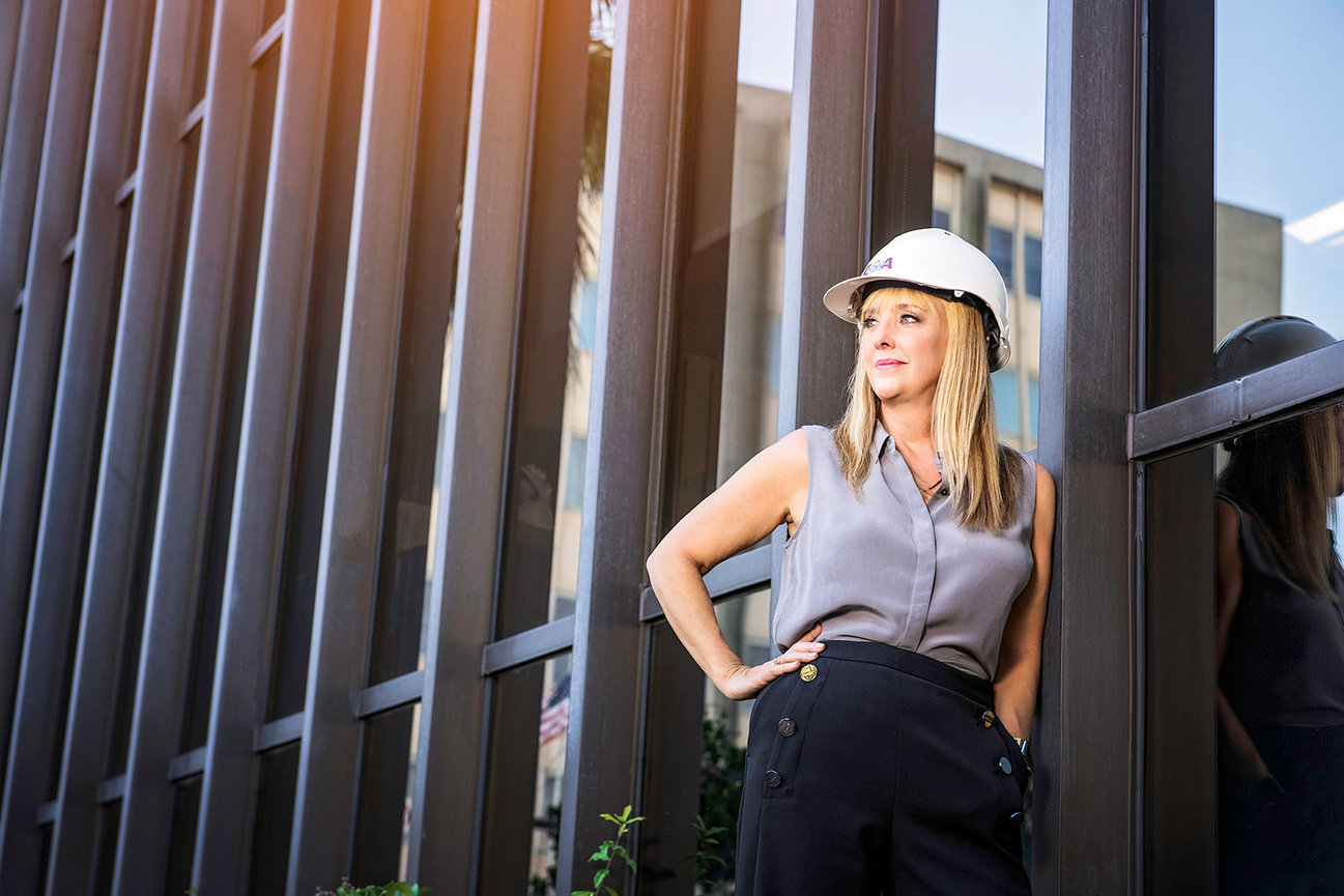 Woman in a hard hat stands confidently outside a modern building, reflecting professionalism in the construction industry.