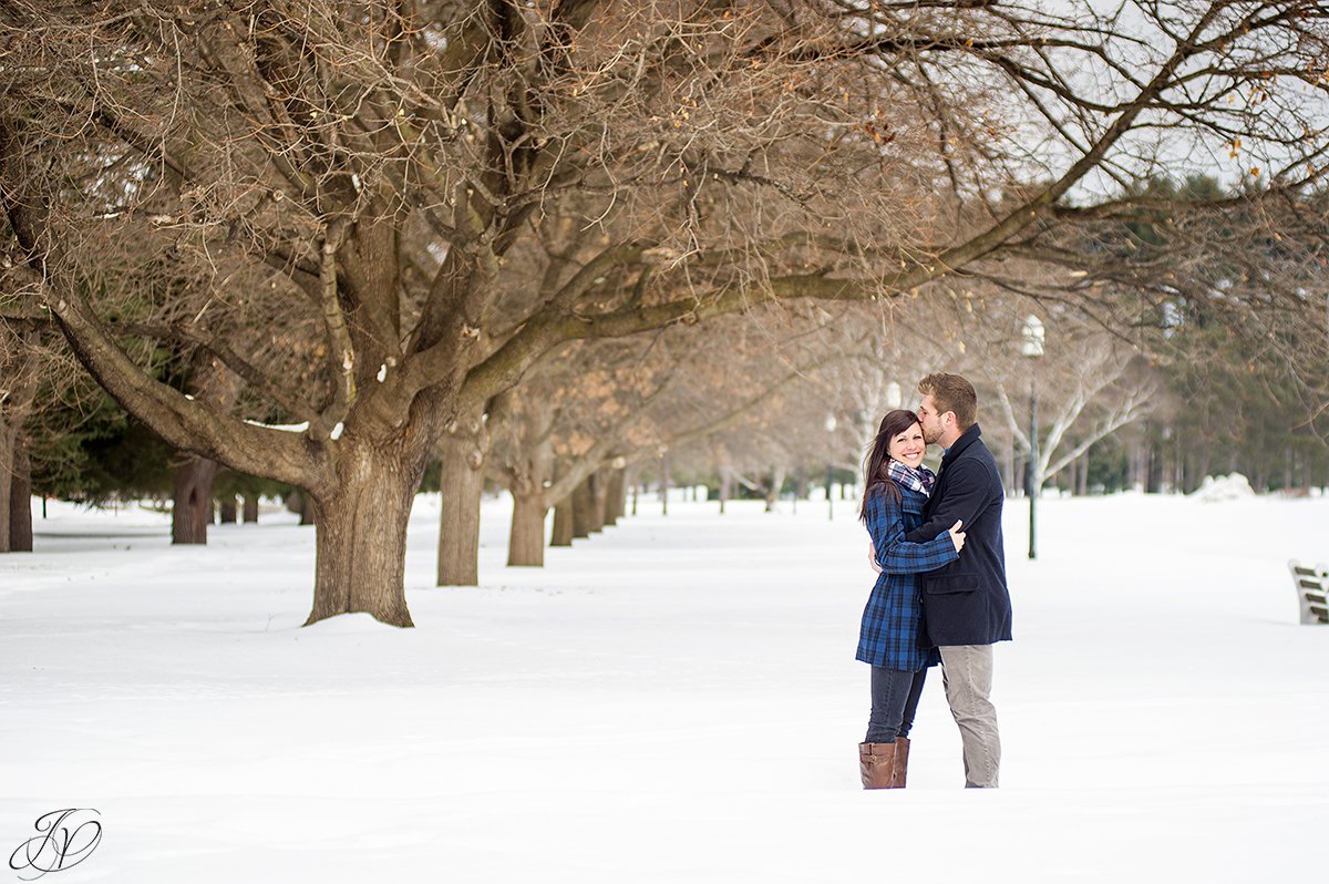winter photo of engaged couple near row of trees