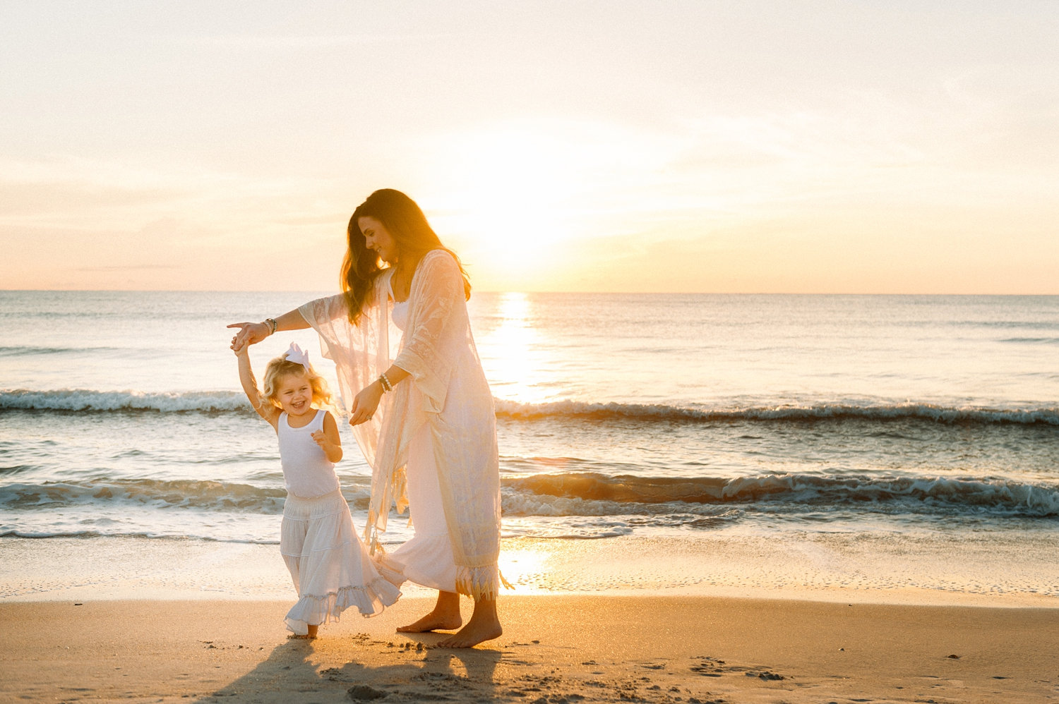 mother with long brown hair twirling her curly haired blonde little girl