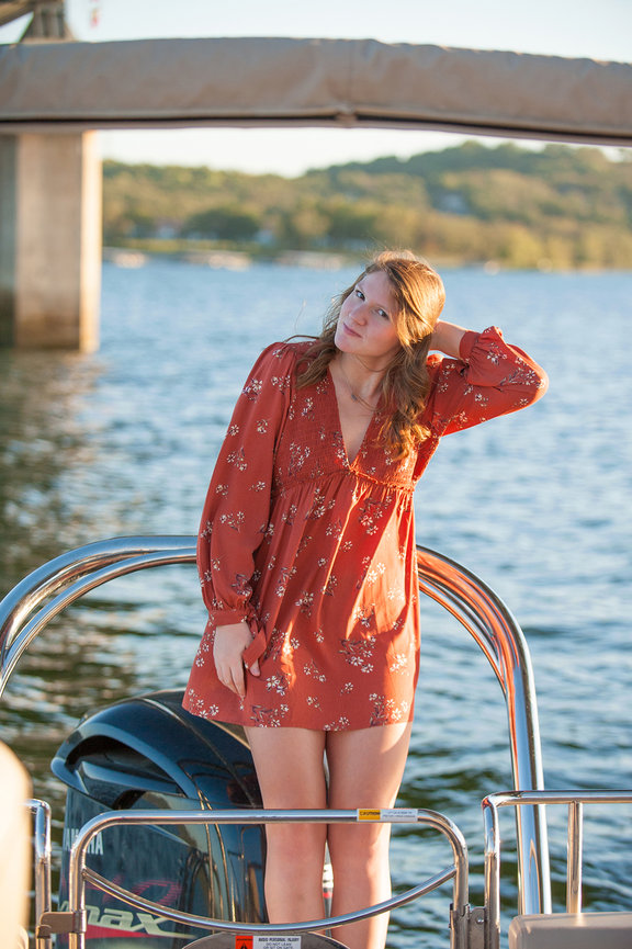 pretty senior girl in orange dress sitting on shore of Table Rock Lake posing for Senior portraits