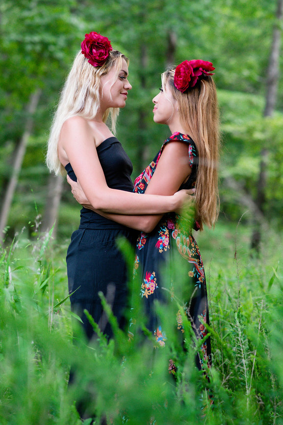 Two women with floral headbands embrace in a lush green forest setting.