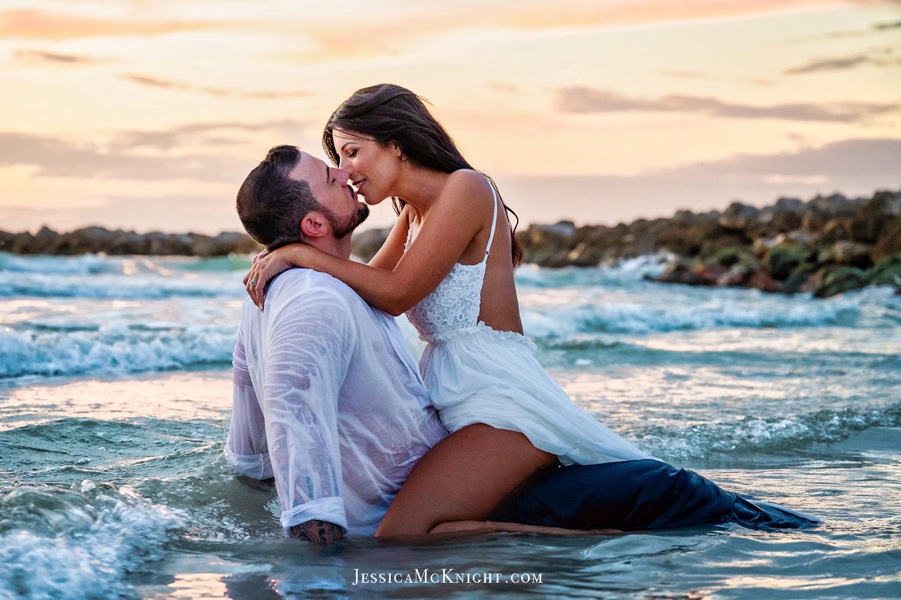 Couple embracing in ocean waves at sunset, showcasing a romantic moment.