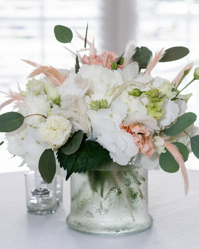 Elegant floral arrangement in a glass vase, featuring white hydrangeas, pink carnations, and greenery.
