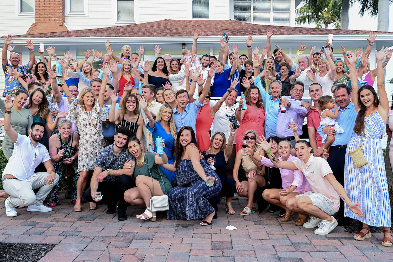 A large, cheerful group of people posing together with drinks, celebrating outdoors.