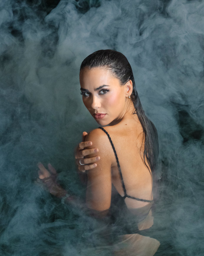 Woman with wet hair, wearing a black outfit, looking back through a misty, smoky background.