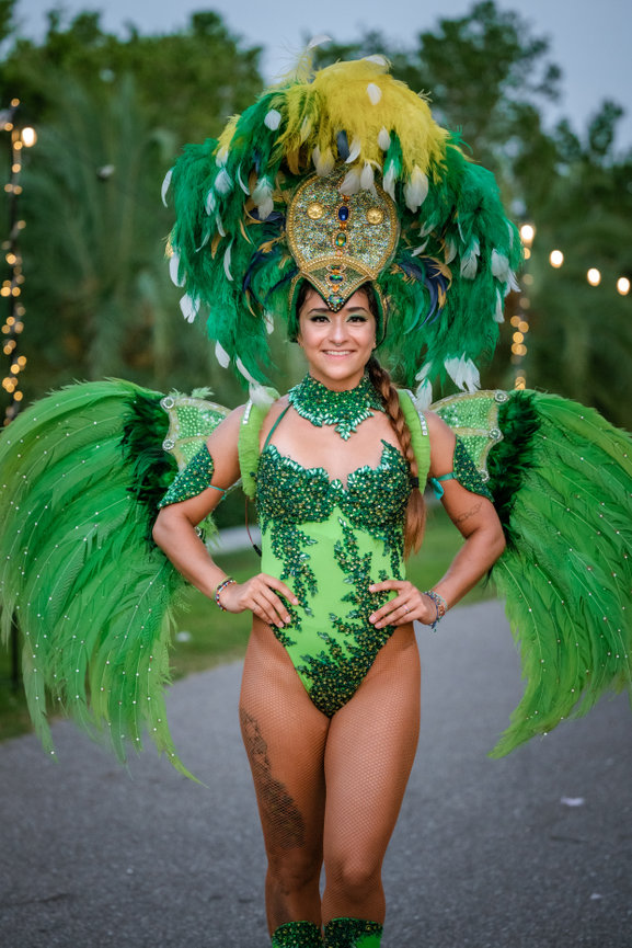 A performer in a vibrant green feather costume poses confidently, featuring intricate details and sparkling embellishments.