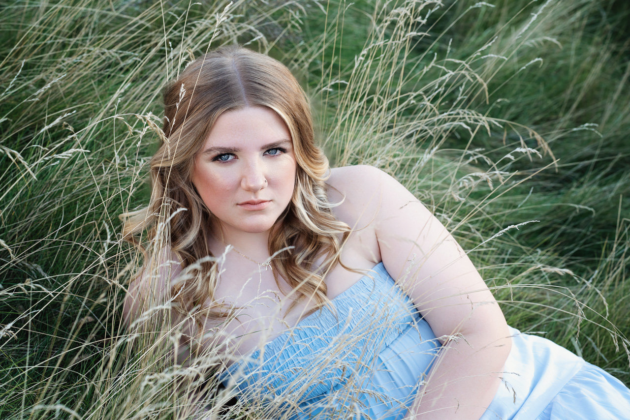 Senior picture of a girl in a blue dress laying in tall grass in Minneapolis Minnesota