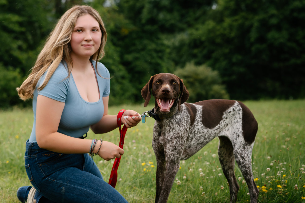 senior girl smiling  in the grass with her dog wearing a blue shirt and jeans