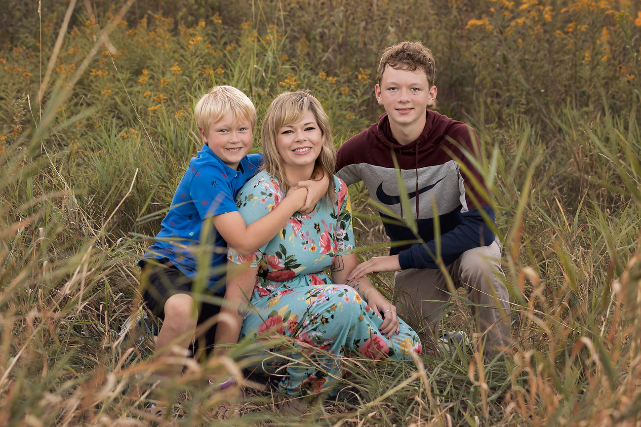 A woman in a floral dress with two boys in a field of tall grass.