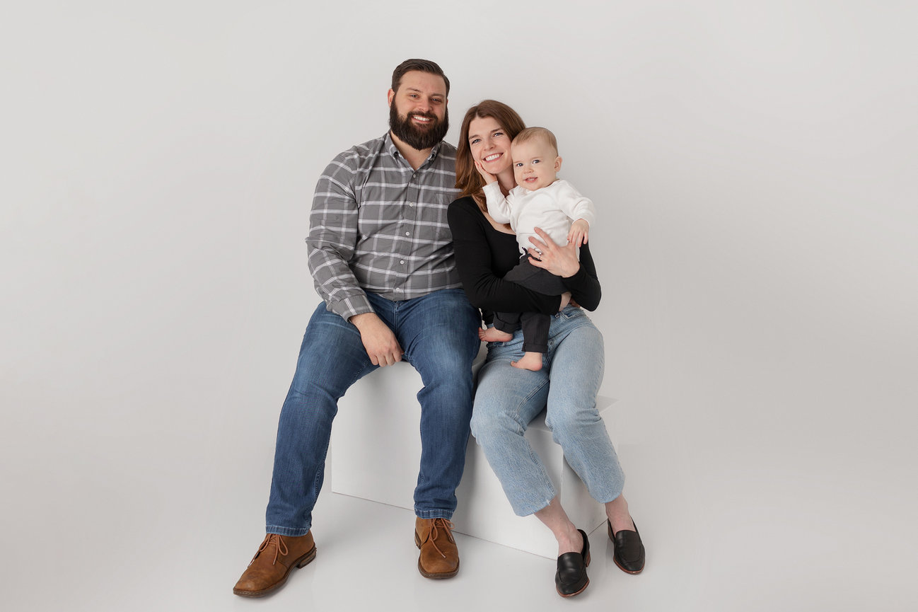 A smiling family of three, sitting together against a plain background.