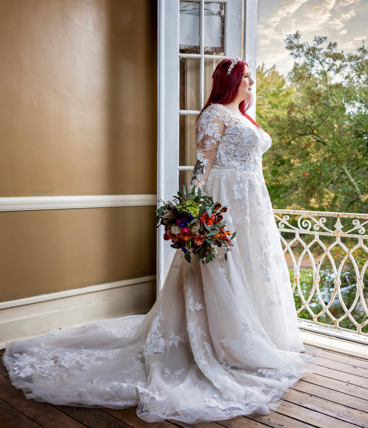 Bride standing near a window in an elegant lace gown, holding a colorful bouquet before her traditional wedding ceremony captured by Fairhope wedding photographer Dixon Creative Images