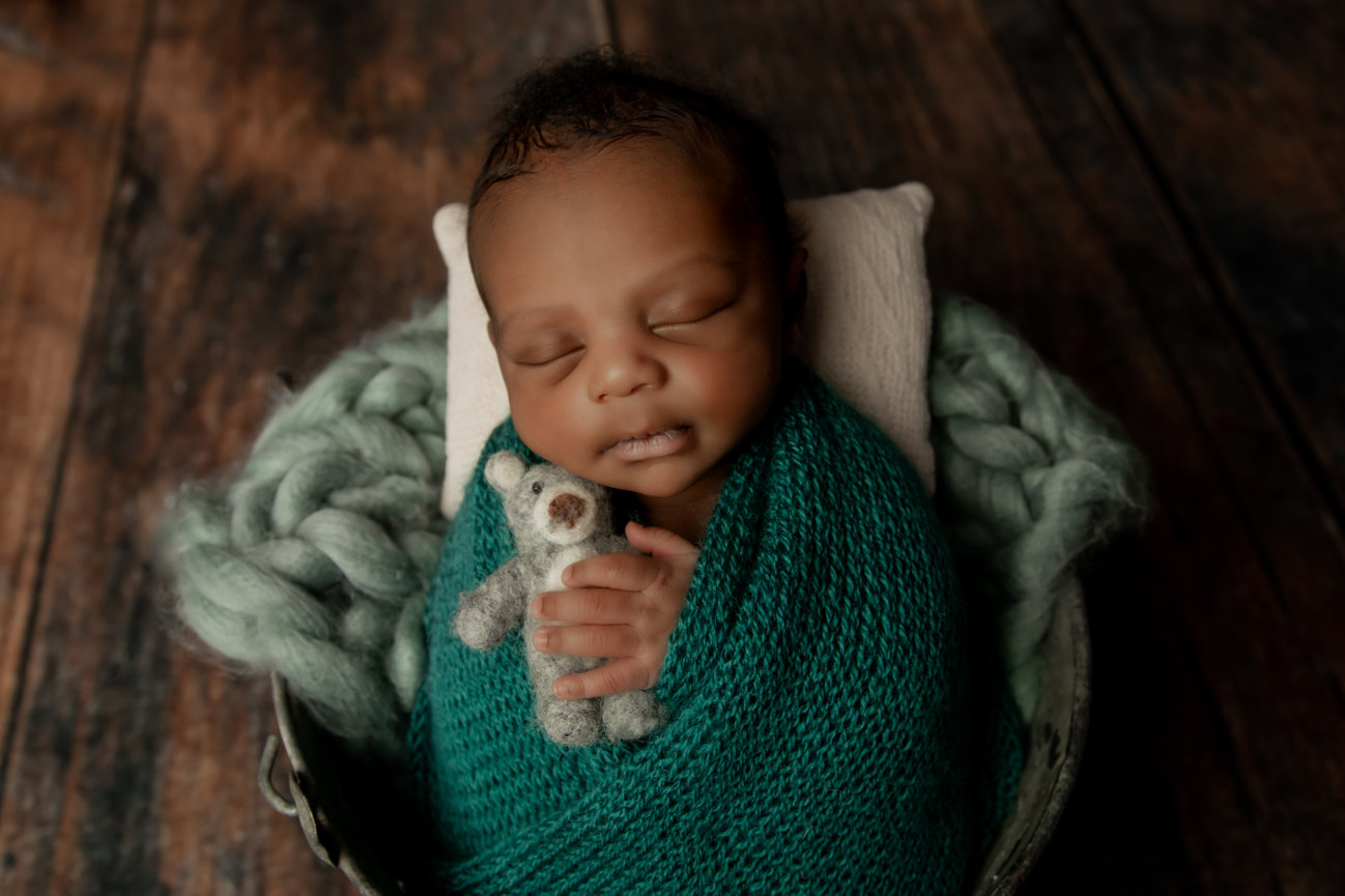 Newborn wrapped in green with a teddy bear