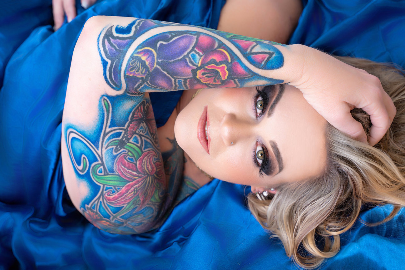 Tattooed woman reclining in blue fabric, with gorgeous blue eyes.