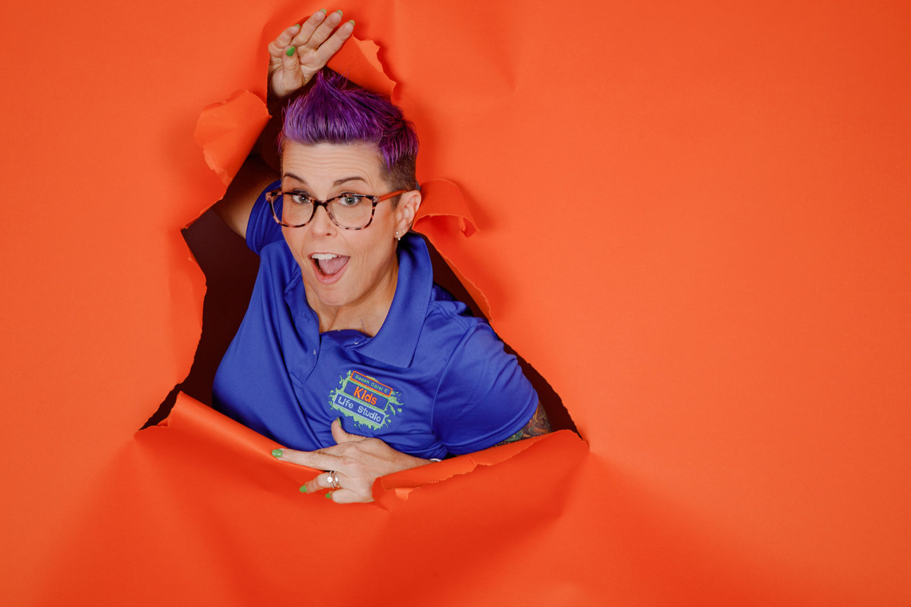 spunky woman with short purple hair tearing through orange paper background