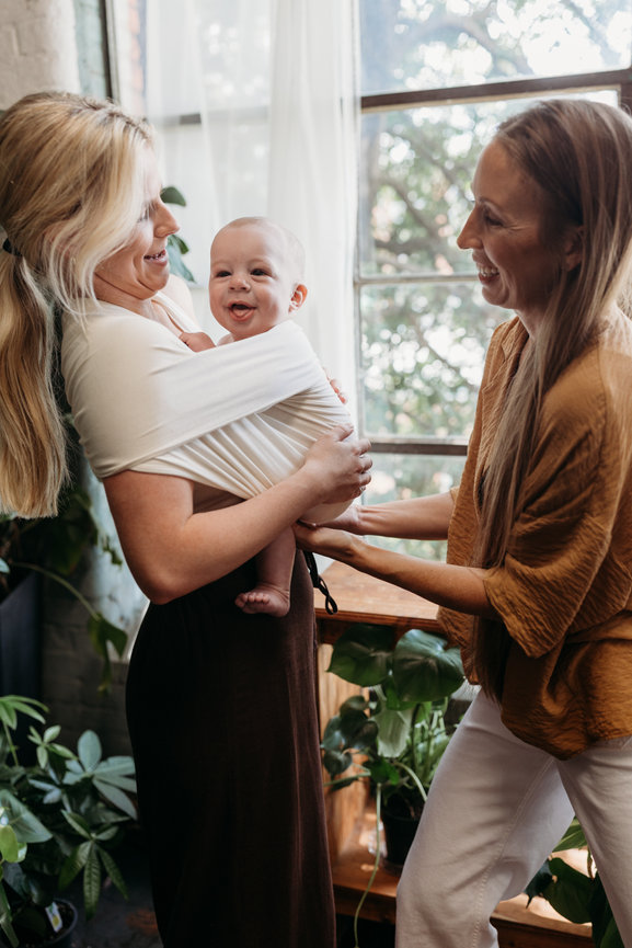 Woman holding baby in baby carrier is assisting by another woman in Huntsville Alabama greenhouse