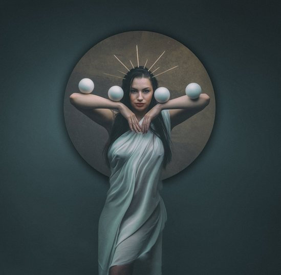 Woman with a halo effect, holding spheres, draped in a white cloth.