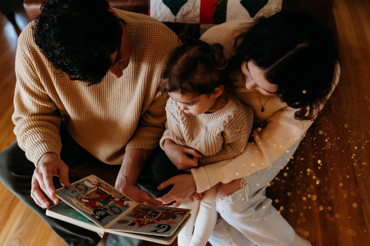 Three people huddled together reading a colorful book indoors from above.