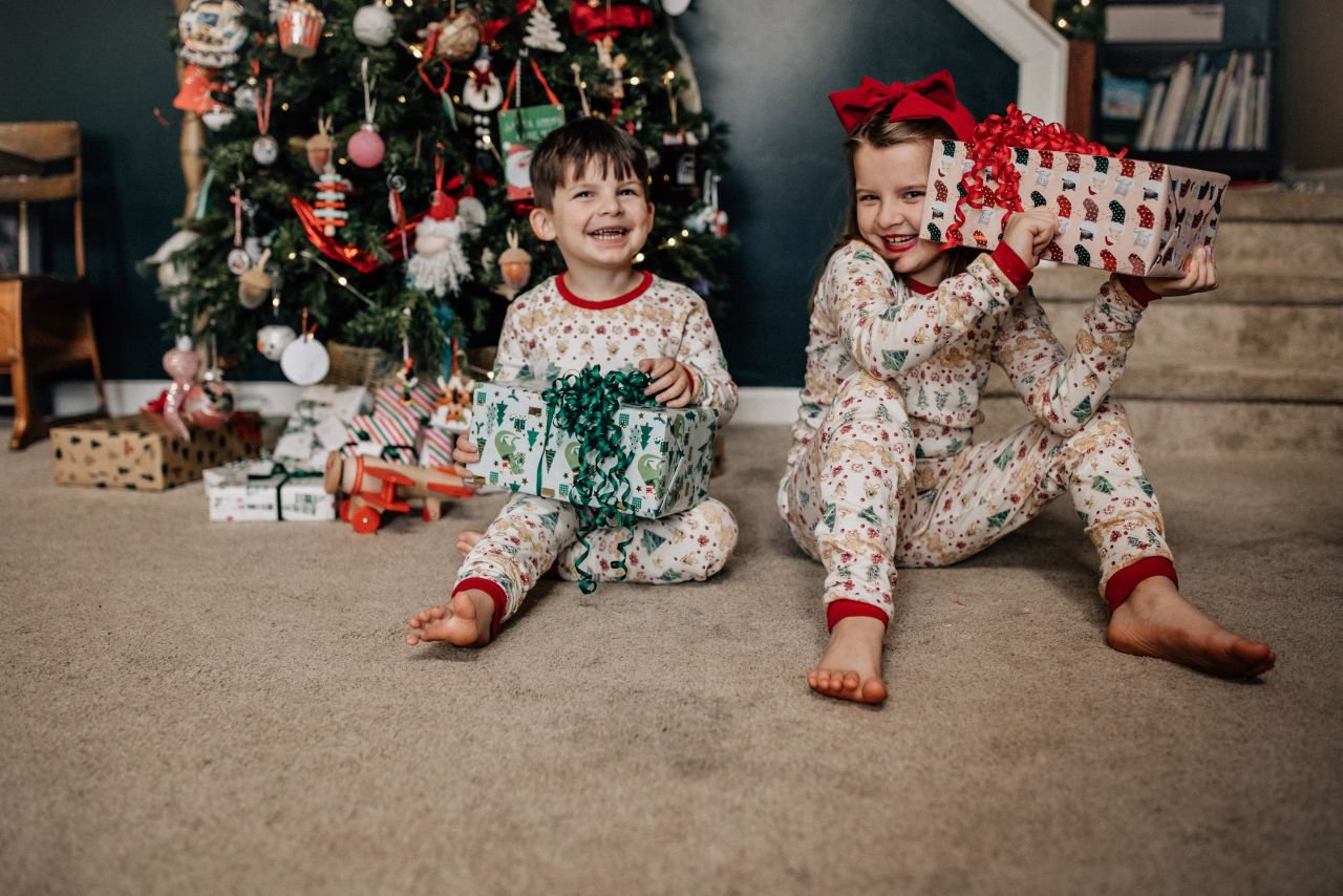 Children in matching pajamas sitting by a decorated Christmas tree with wrapped gifts