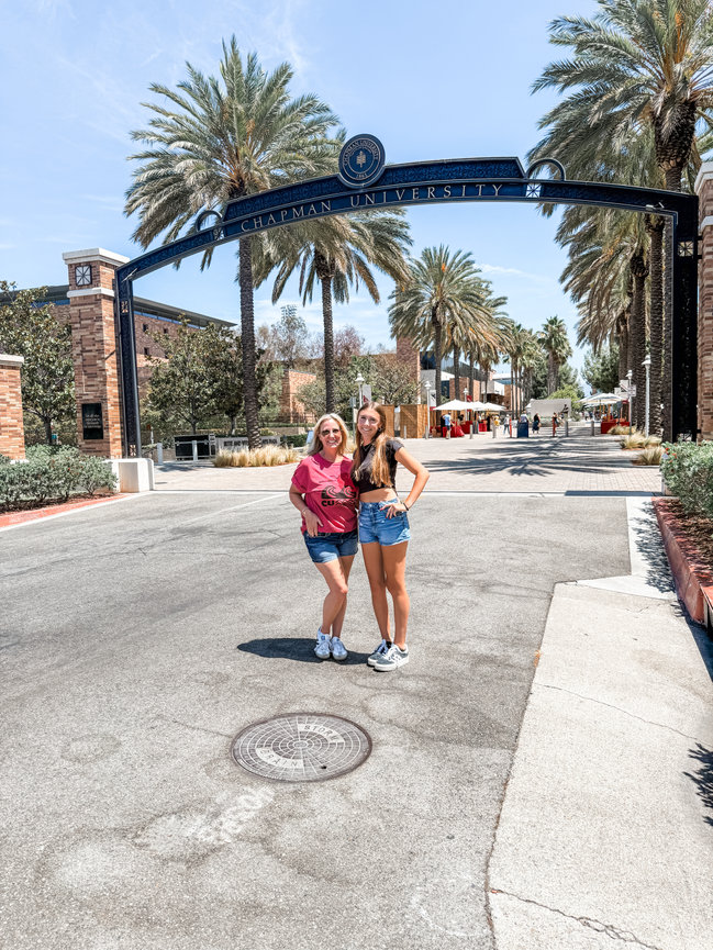 Two people smiling and standing in front of the Chapman University entrance with palm trees lining the campus pathway.