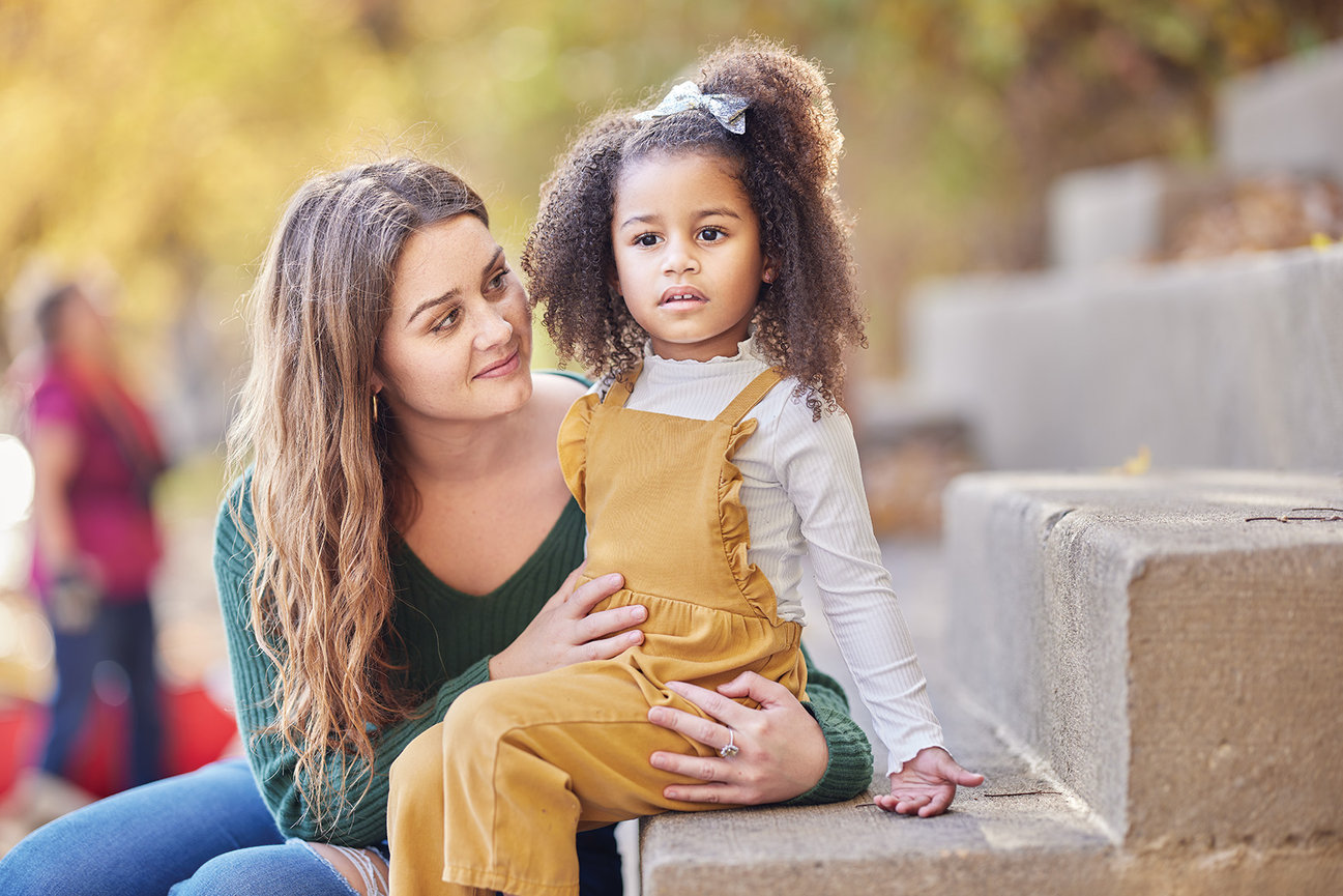 Outdoor portrait of a mother holding her young child seated on a stone step, captured in soft natural light with a warm and connected feel