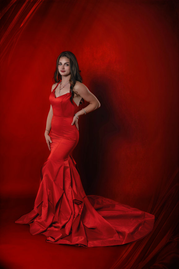 Woman in a red gown posing against a red studio background