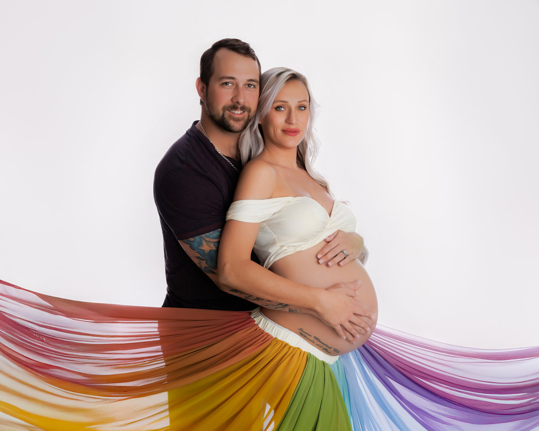 Pregnant couple posing with rainbow fabric in a studio portrait