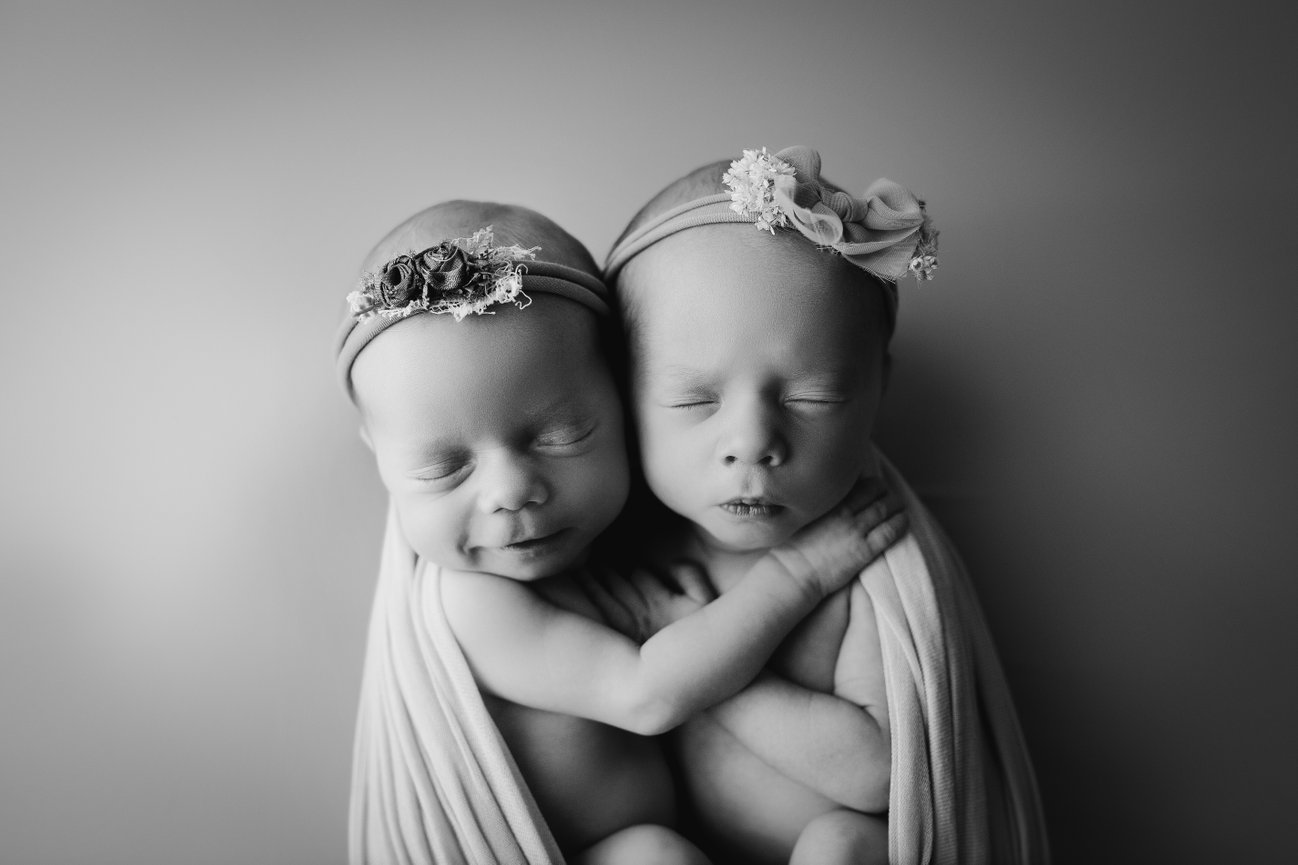 twin newborn girls hugging each other while swaddled at a newborn session
