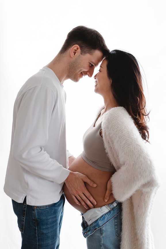 Pregnant couple touching foreheads and smiling against a white background