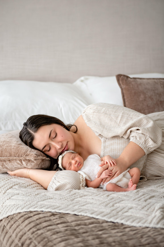 Mother sleeping with newborn baby on a bed, embracing the infant in a cozy bedroom