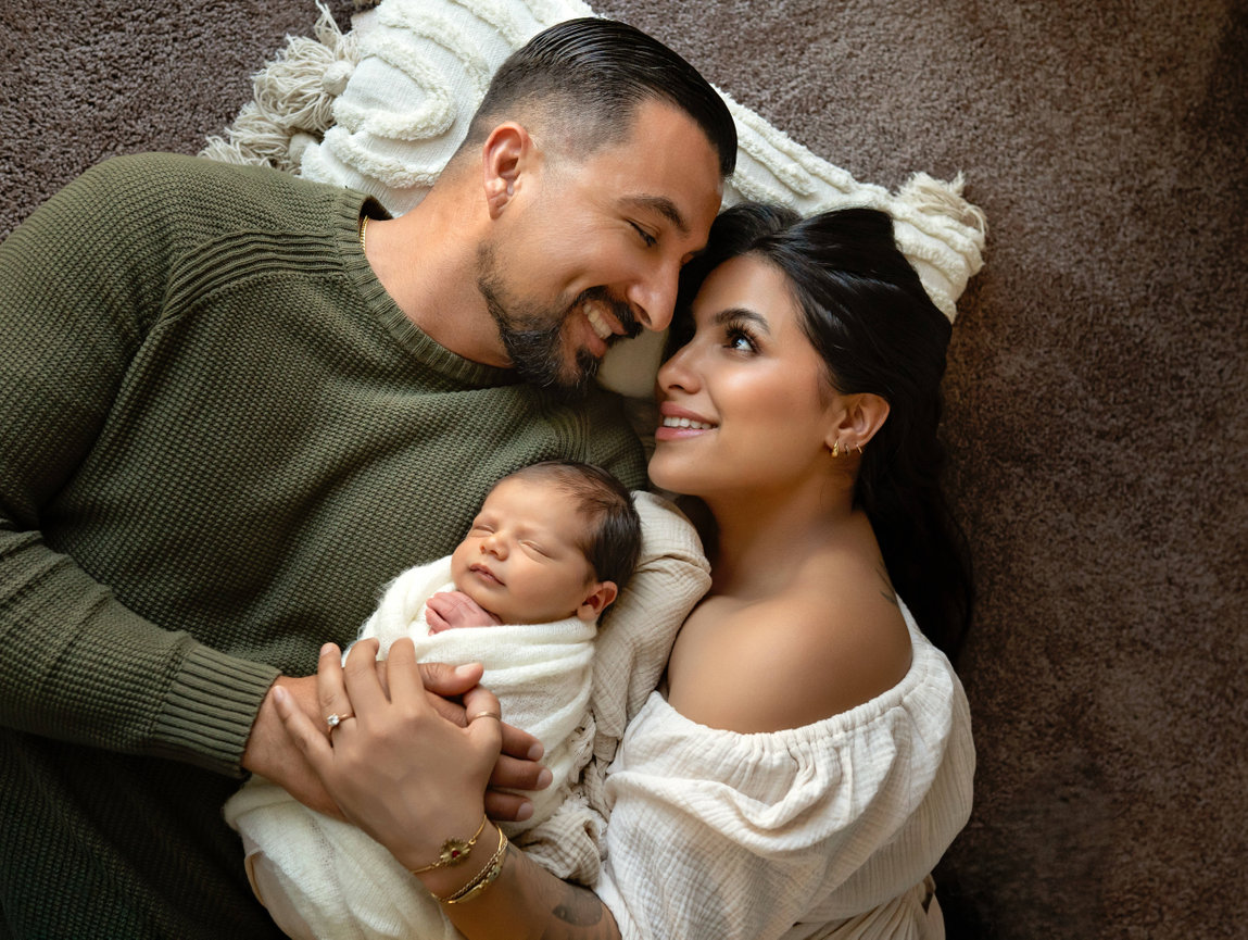 Sleeping parents cuddling their newborn baby on a soft blanket