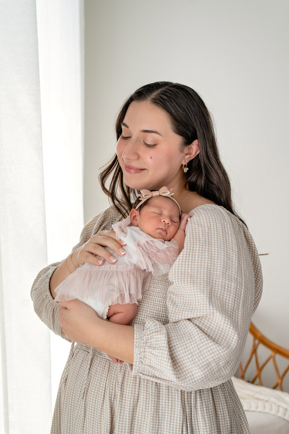 Mother holding sleeping newborn baby in a soft pink dress indoors- studio hillcrest