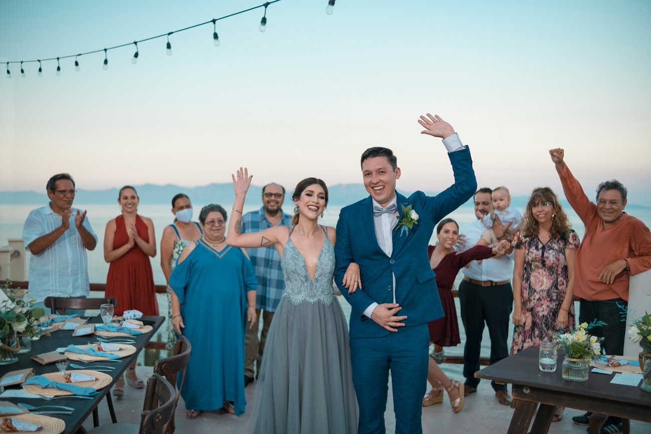 Wedding guests cheer and raise their glasses at an outdoor reception.