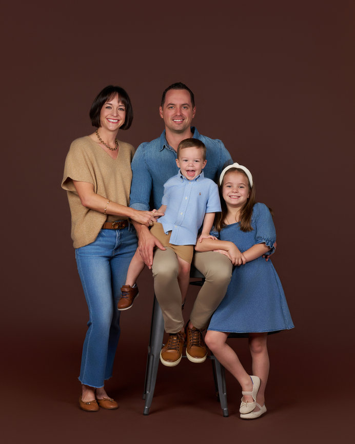 Classic studio family portrait of parents with two young children against a warm brown background, photographed by a Sherman TX family photographer