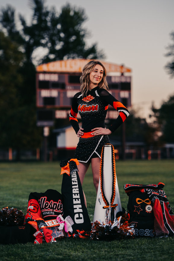 Woman in a sports uniform standing on a field with sports gear nearby.