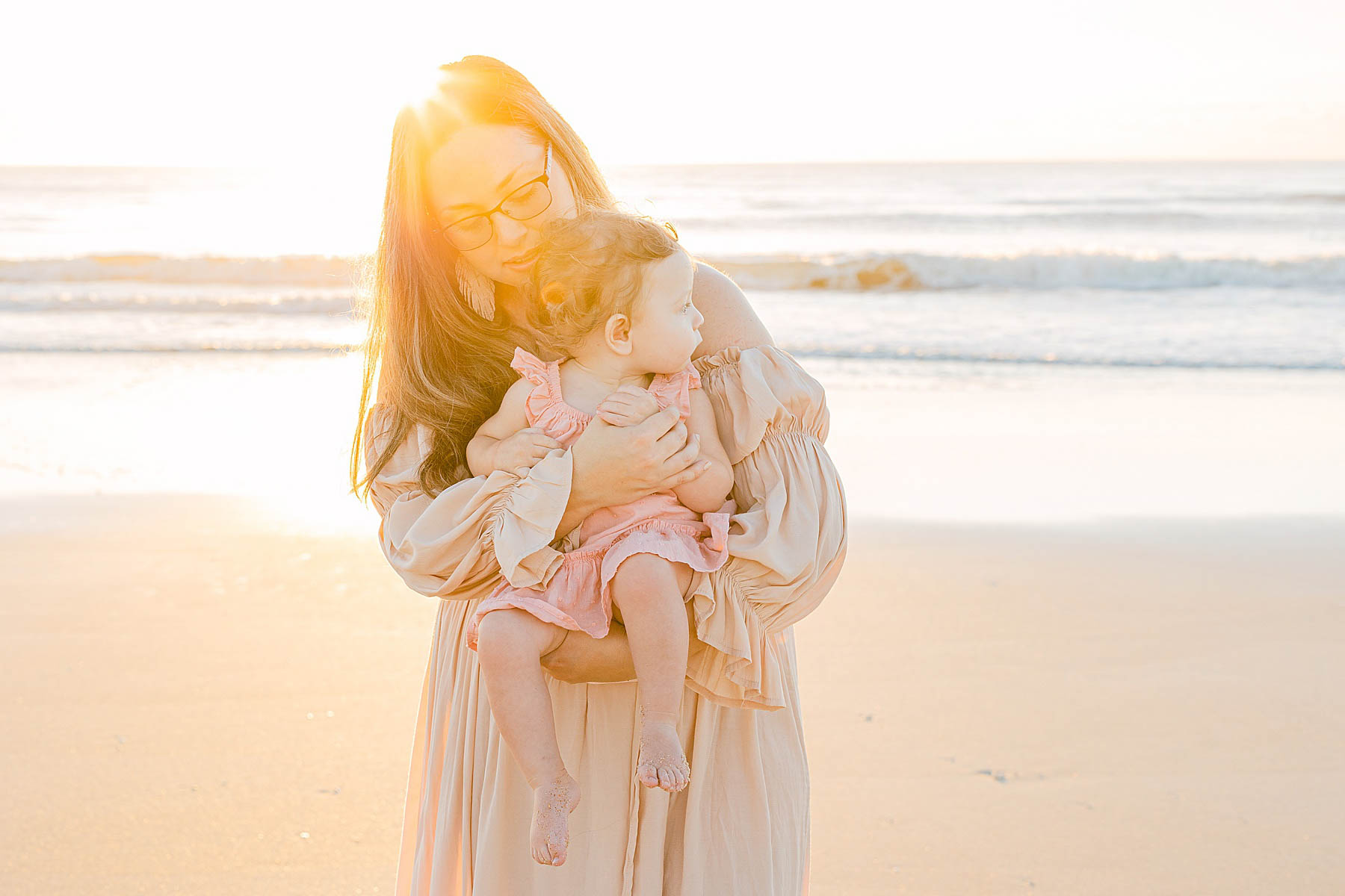 woman wearing sun hat holding baby girl on the beach at sunrise