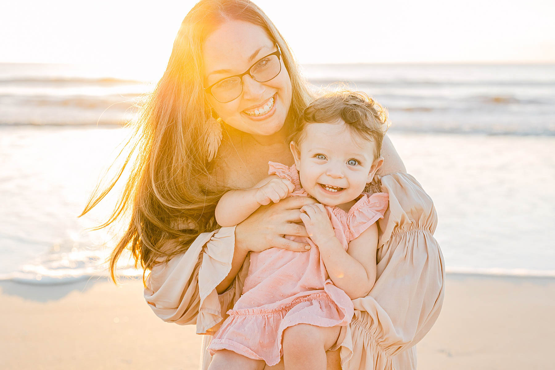mom holding baby girl on the beach at sunrise smiling