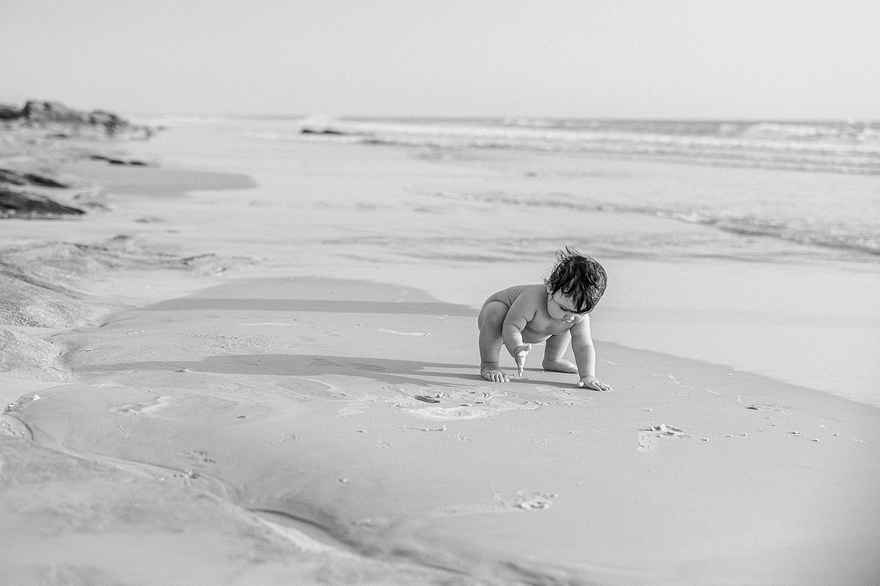 naked baby on the beach in black and white photo