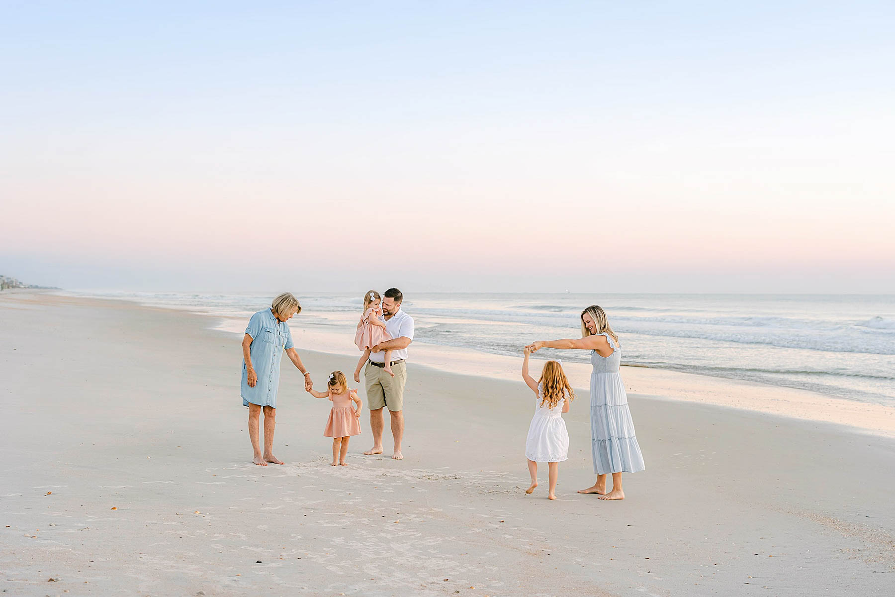 a family dancing at sunrise on the beach wearing pastel colors