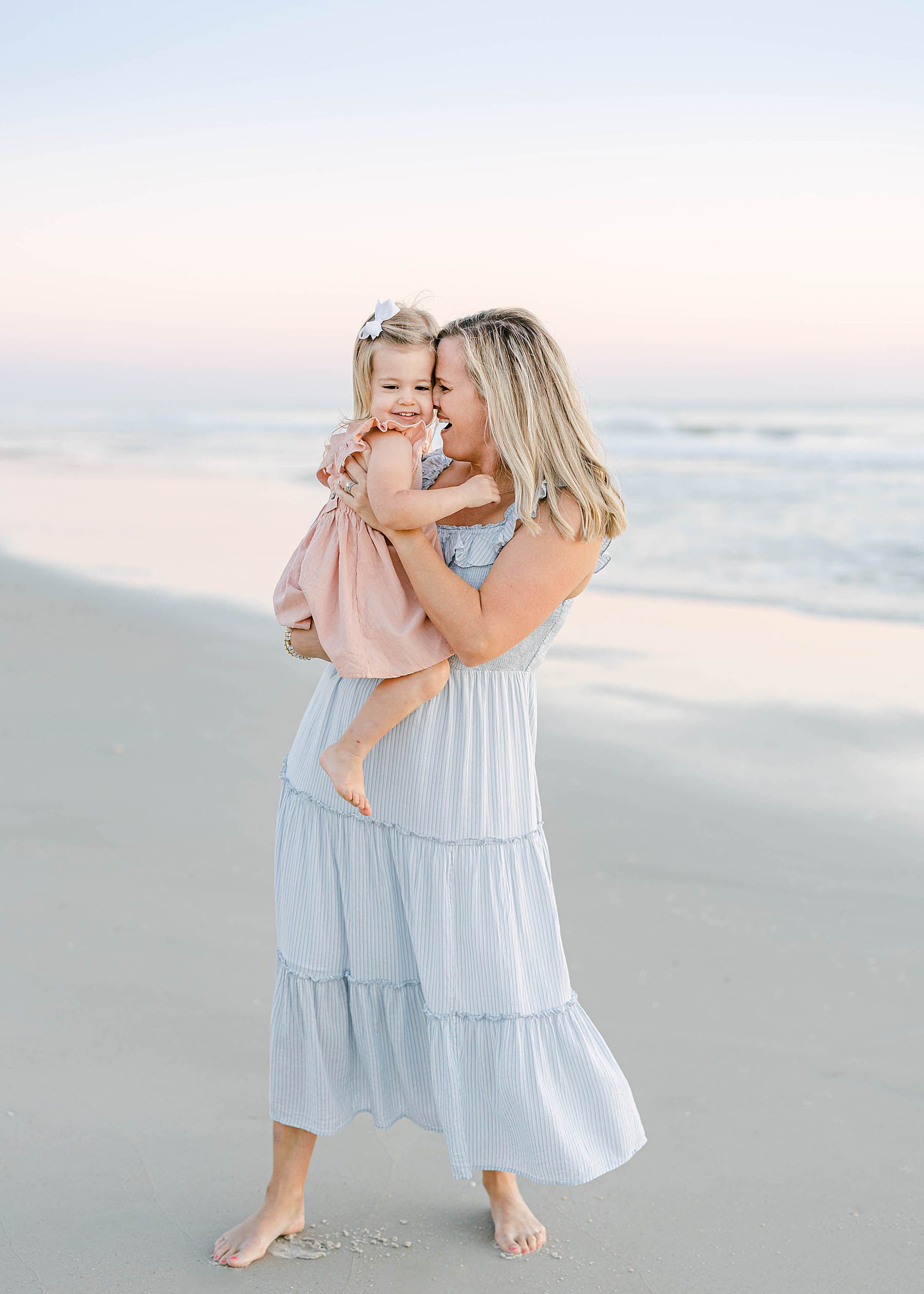 woman wearing a blue dress holding a baby girl on the beach at sunrise in ponte vedra