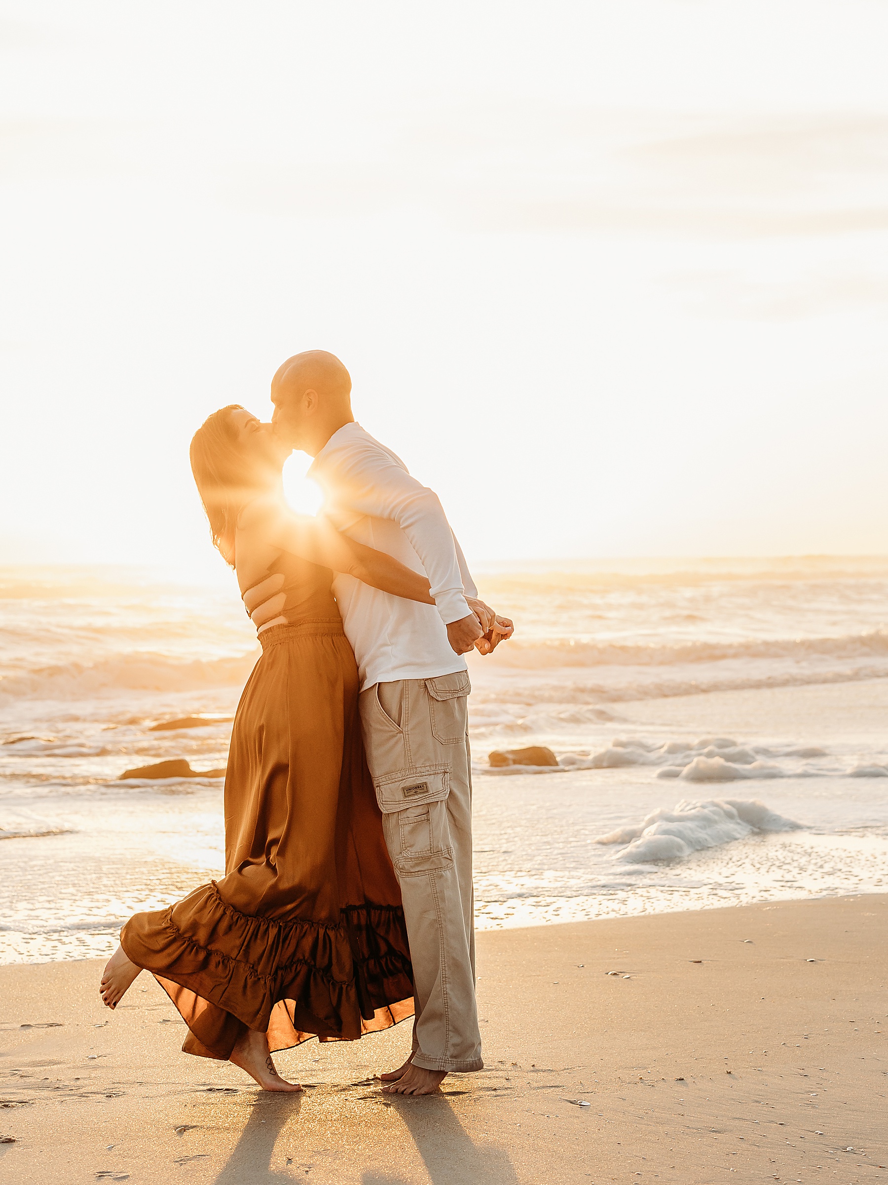 man and woman kissing against the sunrise on the beach