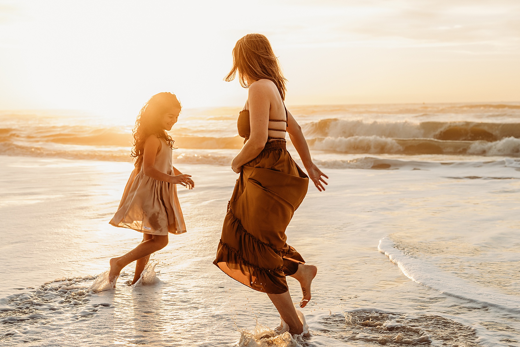 woman in orange maxi dress chasing little girl on the sand at sunrise