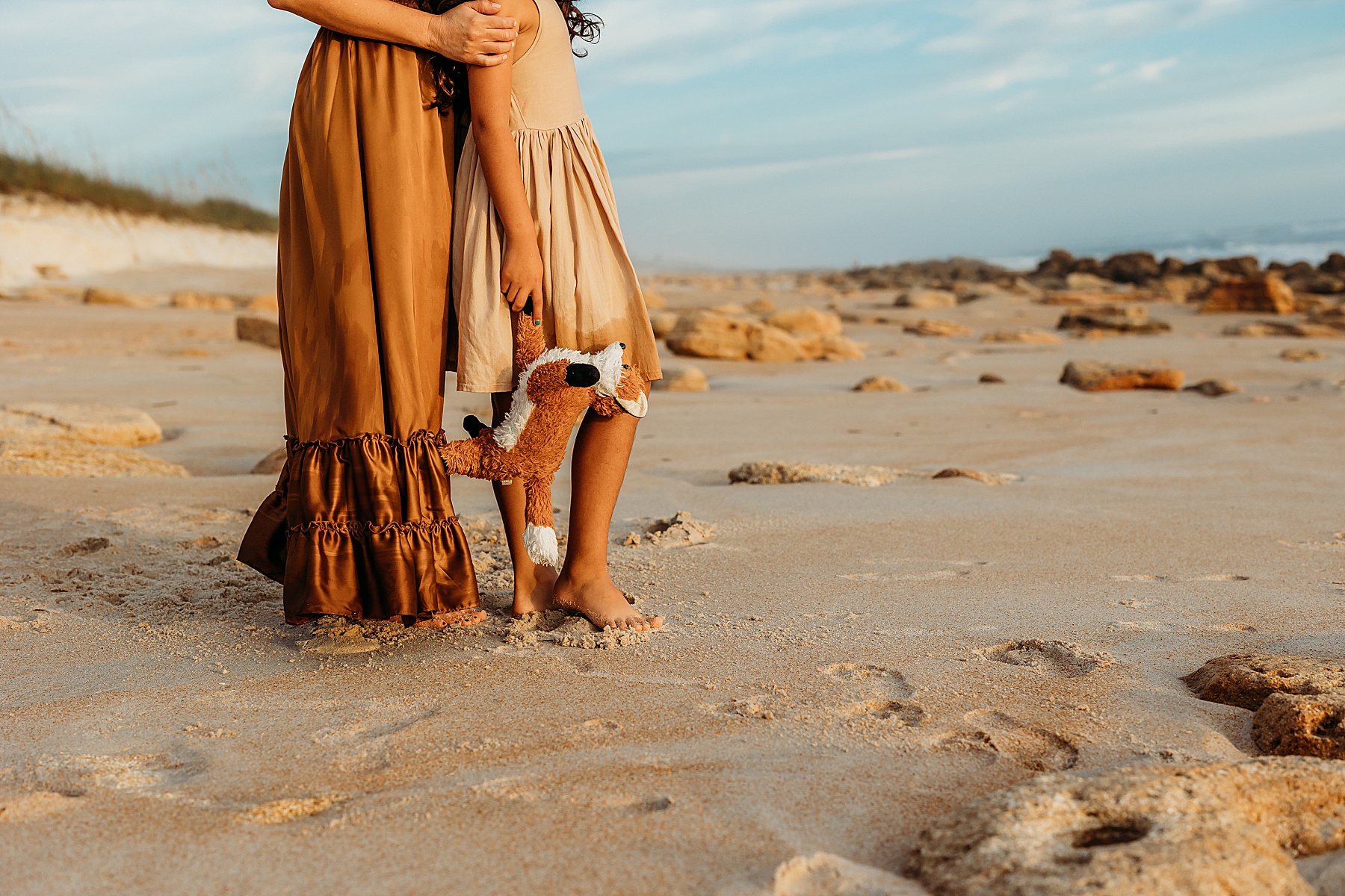 little girl holding toy fox on the beach at sunrise wearing tan dress
