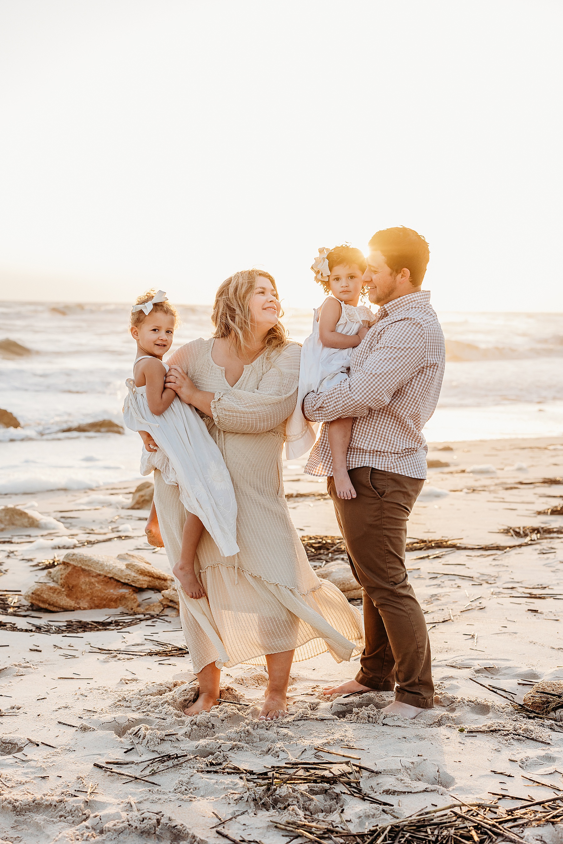 family standing on the beach at sunrise holding little girls dressed in white dresses