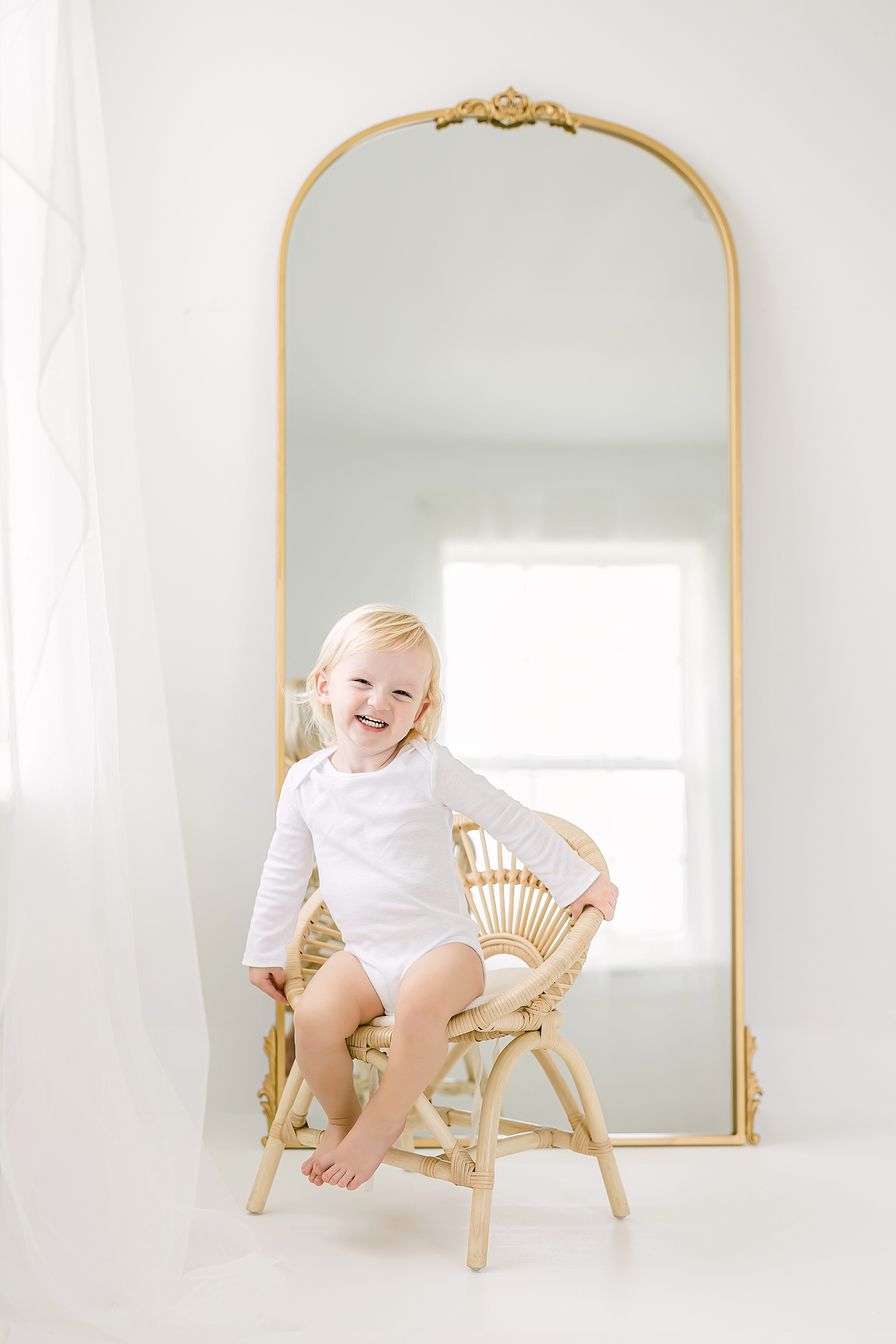 natural light and airy studio baby milestone photo of baby boy in white sitting on chair in front of gold mirror