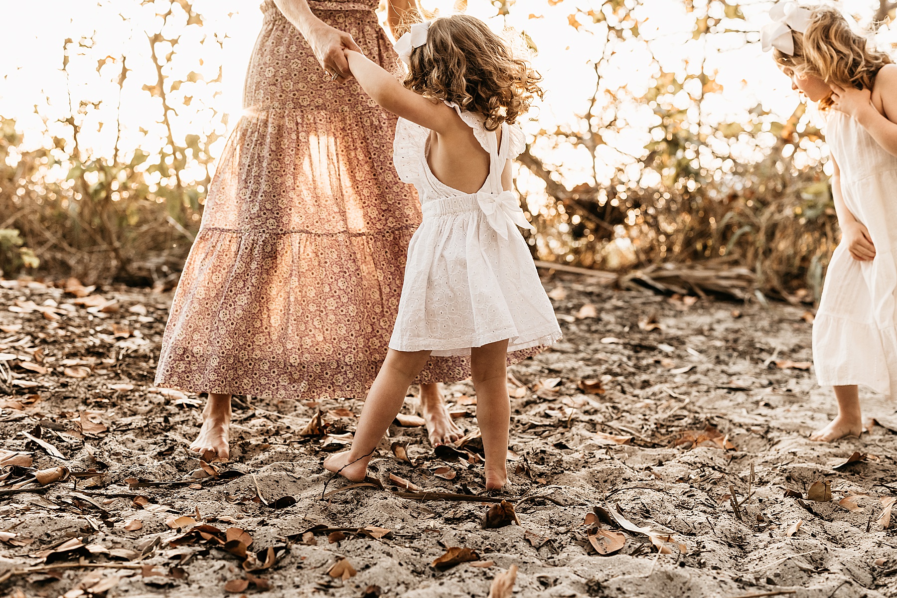 woman in long maxi dress dancing at sunset on the beach with little girl in white dress