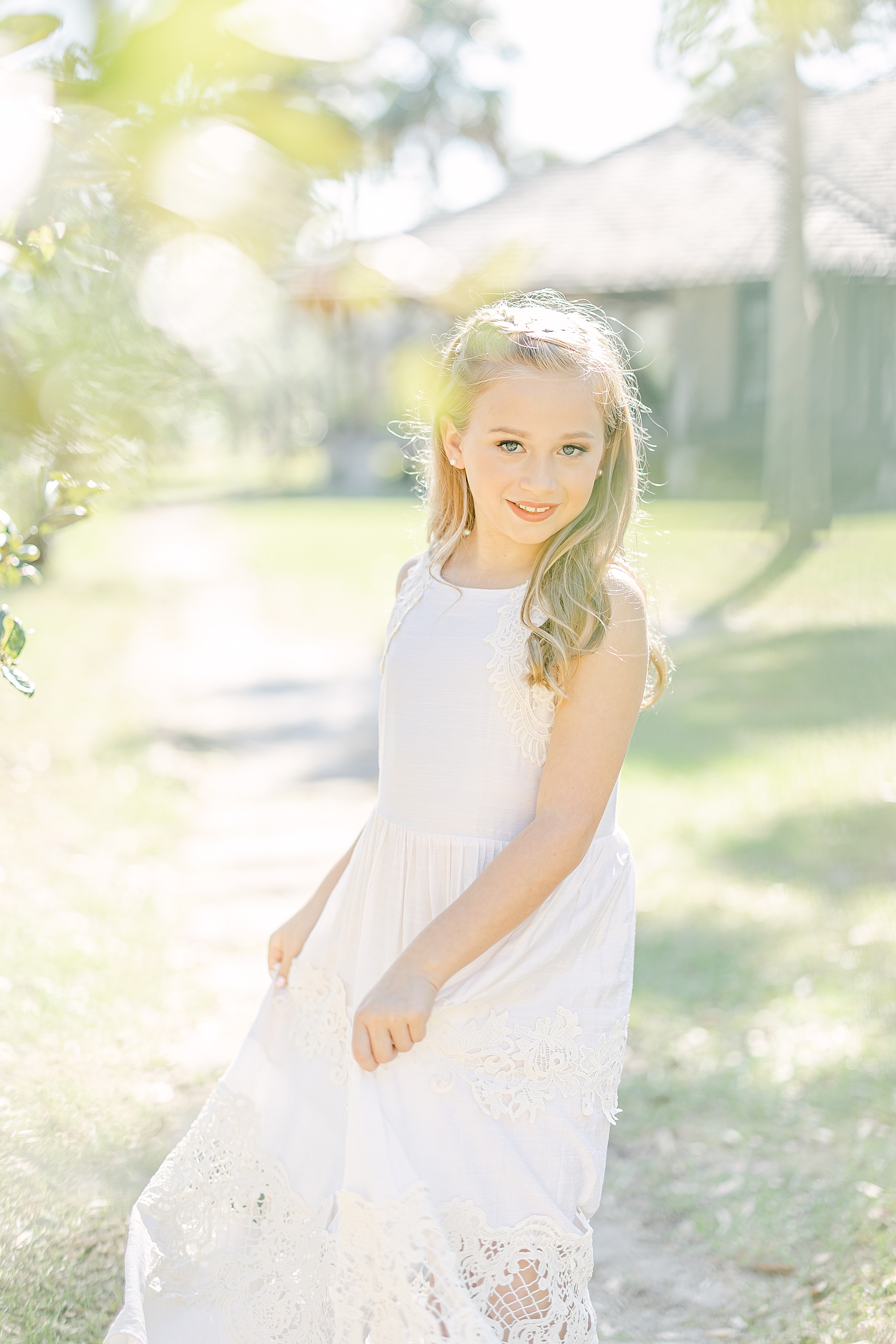 little girl in light and airy white dress with long hair dancing in the sunlight at Princess Place Preserve