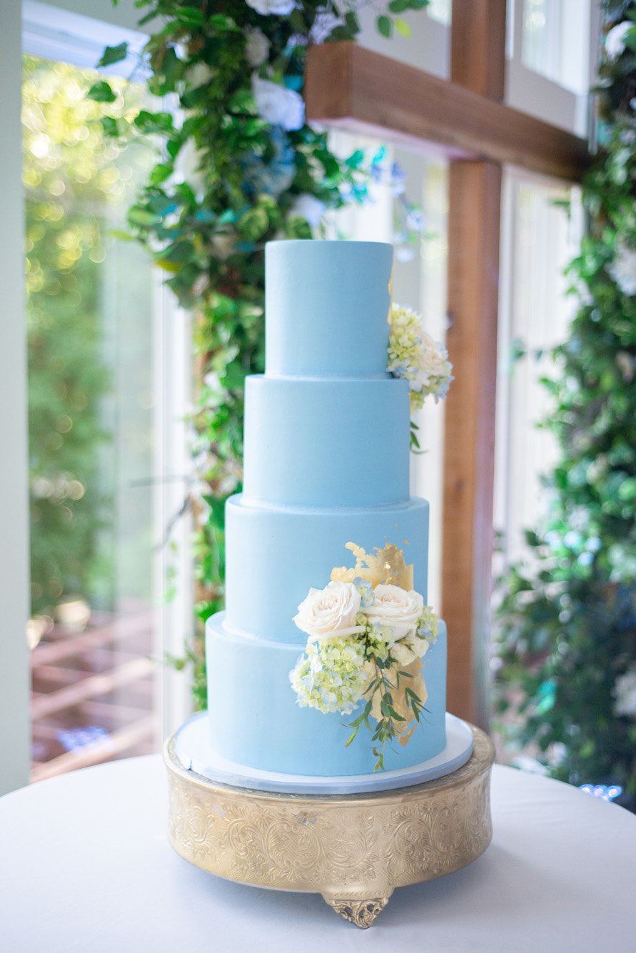 French blue wedding cake with gold foil and fresh flowers on a gold pedestal.